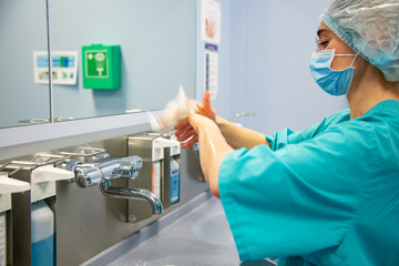 Female Surgeon in a medical mask and in a suit in the hospital washing thoroughly her hands before...