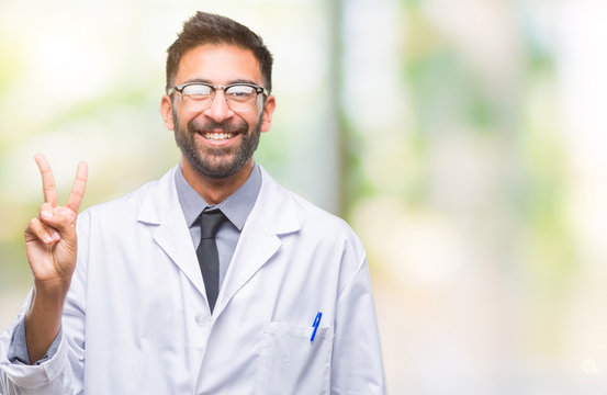 Adult hispanic scientist or doctor man wearing white coat over isolated background smiling with happy face winking at the camera doing victory sign. Number two.