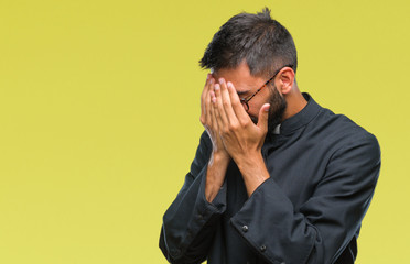 Adult hispanic catholic priest man over isolated background with sad expression covering face with...