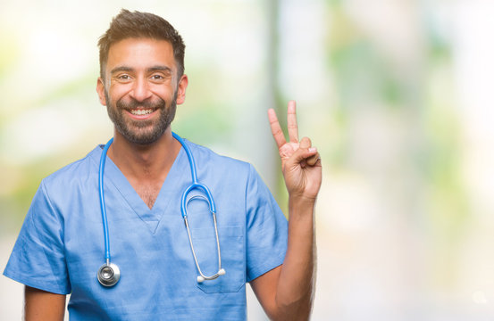 Adult hispanic doctor or surgeon man over isolated background smiling with happy face winking at the camera doing victory sign. Number two.