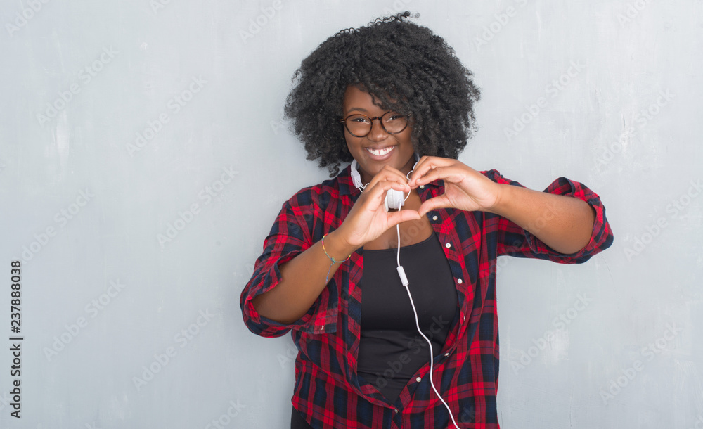 Canvas Prints Young african american woman over grey grunge wall wearing headphones smiling in love showing heart symbol and shape with hands. Romantic concept.