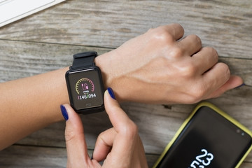 Woman measuring blood pressure with modern smart watch against wooden table