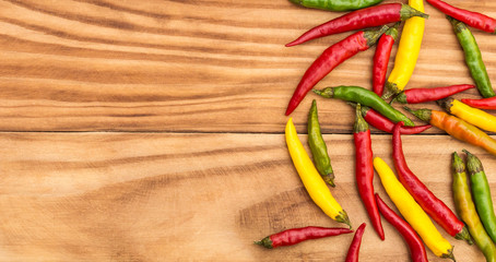 Small colorful chilli peppers on wooden background with space for text.