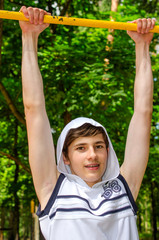 Fototapeta premium teenager boy in a white sleeveless shirt pulls up on a horizontal bar