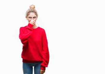 Young beautiful blonde woman wearing red sweater and glasses over isolated background smelling...