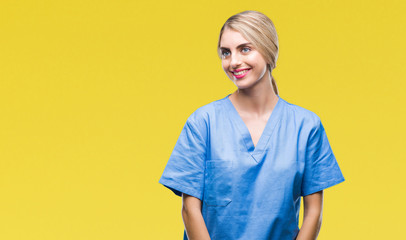 Young beautiful blonde doctor surgeon nurse woman over isolated background looking away to side...