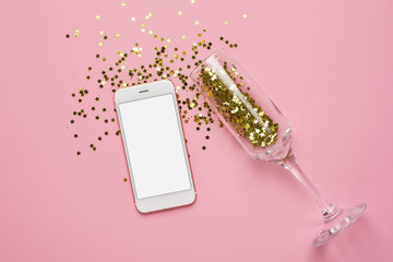 Mobile phone and champagne glasses with golden stars confetti on pink color paper background minimal style