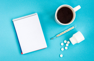 Mug of tea, thermometer and pills on blue background with notebook for recipe. Disease concept. 