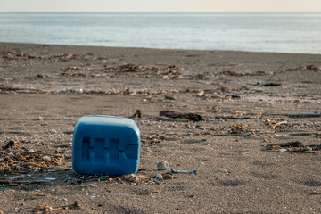 Blue plastic container and more little plastic trash in the sand of the beach, near the shore line.