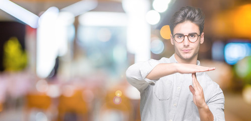 Young handsome man wearing glasses over isolated background Doing time out gesture with hands, frustrated and serious face