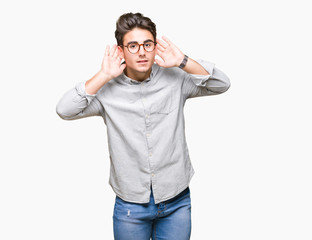 Fototapeta premium Young handsome man wearing glasses over isolated background Trying to hear both hands on ear gesture, curious for gossip. Hearing problem, deaf