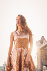 The divine young woman in beautiful dress standing outdoors and looking aside