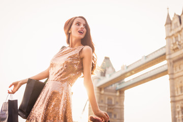 The divine young woman standing outdoor and holding the shopping bag in hand and looking aside