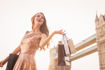 The smiling divine young woman standing outdoor and holding the shopping bags in hands and looking...