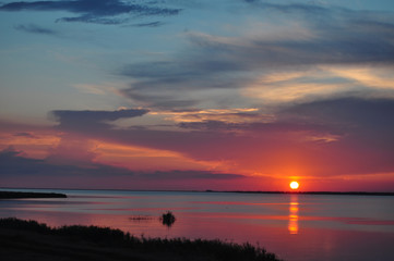Beautiful landscape of golden spot of sun going down on colorful sky reflecting in tranquil water....