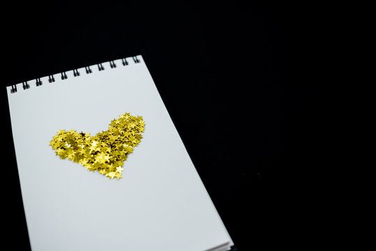 Spiral Notebook, realistic mockup White scetchbook on black abstract background with golden stars confetti.Horizontal top view..