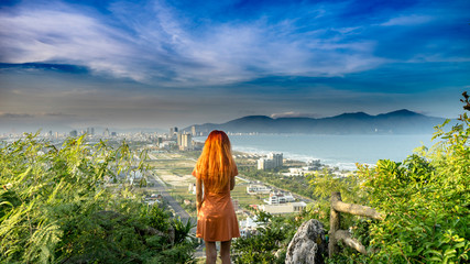 Travel girl with red hair is travelling in Marble Mountains ,staying on the top and watching a view of the Da Nang city on sunset with junles,sea and mountains in Vietnam, travel concept