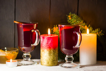 Mulled wine and burning candle on dark background. Christmas mulled wine, cinnamon sticks and honey. Alcohol drink of wine and honey. Festive drink and Christmas tree branches