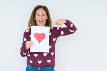 Middle age woman holding card gift with red heart over isolated background very happy pointing with hand and finger