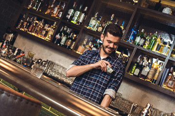 Young bartender standing at bar counter putting banknotes into pocket satisfied