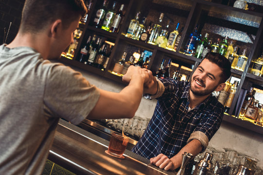 Young bartender standing at bar counter with customer fist bumb cheerful