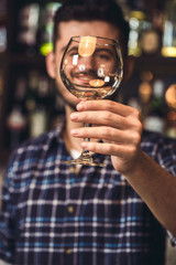 Young bartender standing at bar counter holding glass close-up happy