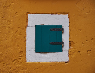 Minimal view of a single centered green shutter, framed in white against a yellow wall.