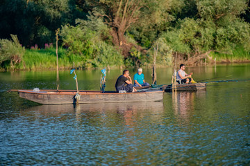 Fototapeta na wymiar Novi Sad, Serbia - August 04, 2018: Danube island (Šodroš) near Novi Sad, Serbia. Fishermans sitting in boat and holding fishing rod.