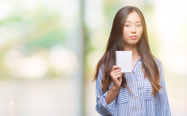 Young asian woman holding notebook over isolated background with a confident expression on smart face thinking serious