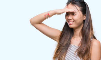 Young asian woman wearing sunglasses over isolated background very happy and smiling looking far...