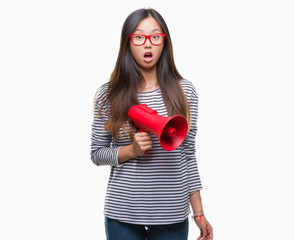 Young asian woman holding megaphone over isolated background scared in shock with a surprise face, afraid and excited with fear expression