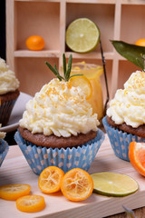 Cupcakes topped with butter cream, slices of kumquat and rosemary surrounded by fruits