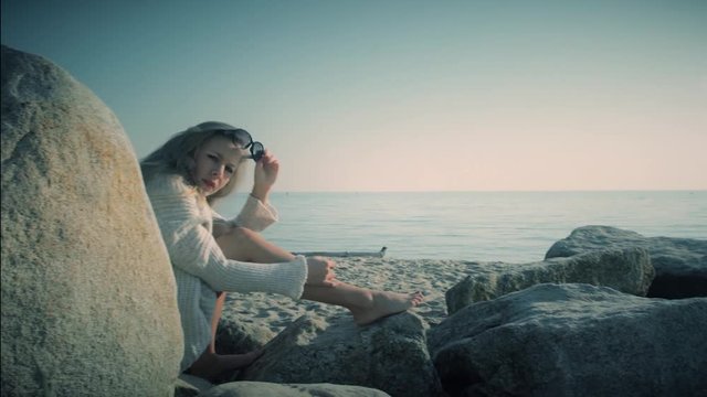 A beautiful woman sitting alone on the rocks at the beach notices a creepy person spying on her and speaks out