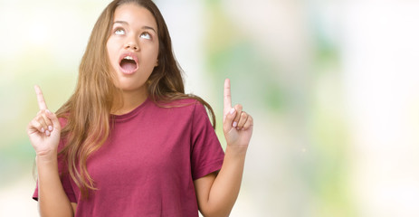 Young beautiful brunette woman over isolated background amazed and surprised looking up and pointing with fingers and raised arms.