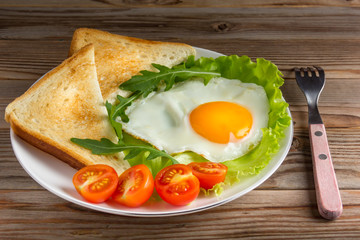 Fototapeta na wymiar fried egg with tomatoes, salad, arugula and triangle toasts on wooden rustic background. Soft focus.