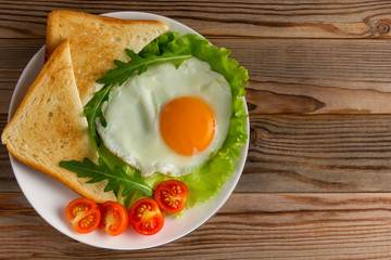fried egg with tomatoes, salad, arugula and triangle toasts on wooden rustic background, with right copy space