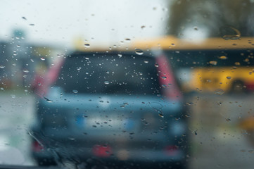 closeup of rain drops on windshield with blurred cars on background