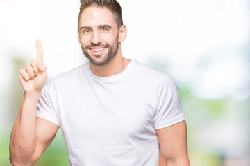 Naklejka premium Young man wearing casual white t-shirt over isolated background pointing finger up with successful idea. Exited and happy. Number one.