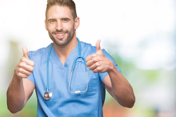 Fototapeta premium Handsome young doctor surgeon man over isolated background success sign doing positive gesture with hand, thumbs up smiling and happy. Looking at the camera with cheerful expression, winner gesture.