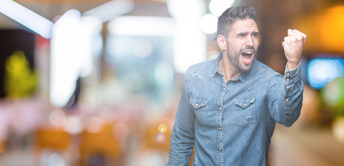 Young handsome man over isolated background angry and mad raising fist frustrated and furious while shouting with anger. Rage and aggressive concept.