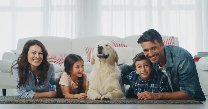 Portrait Of Happy Family With A Dog Having Fun Lying On The Carpet In Living Room In Slow Motion. 