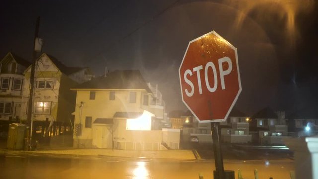 A strong storm bring rain and wind to an empty town at night making a stop sign shake.