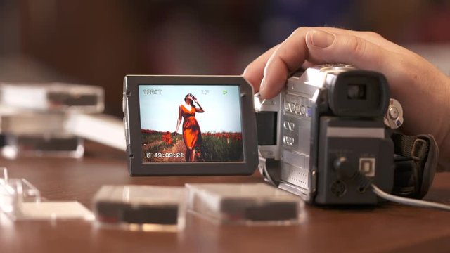 Man watching family home video on LCD screen of digital Mini DV camcorder. Young woman in summer on display of obsolete miniDV video camera.