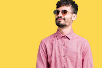 Fototapeta premium Young handsome man wearing sunglasses over isolated background looking away to side with smile on face, natural expression. Laughing confident.