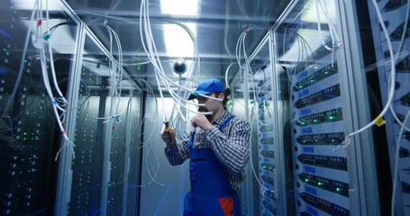 Medium long shot of a technician cutting wires at a data center - Powered by Adobe
