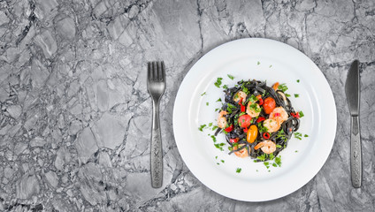 Black squid ink Fettuccine pasta with prawns or shrimps cherry tomatoes, parsley, chili in wine and butter sauce. Top view on granite with copy space.