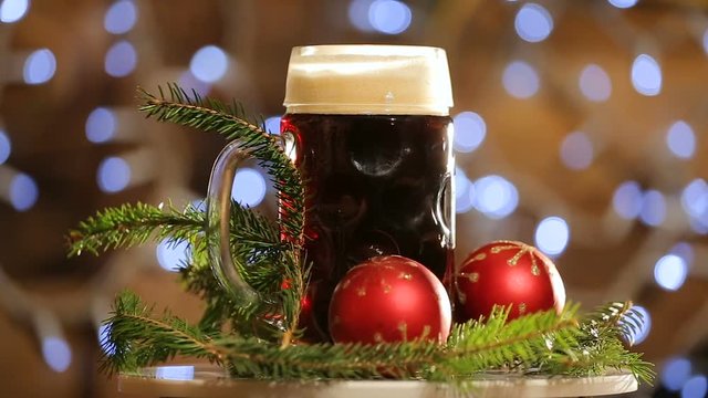 Beer in glass rotate on background with bright lights bokeh. Christmas dark beer presentation.