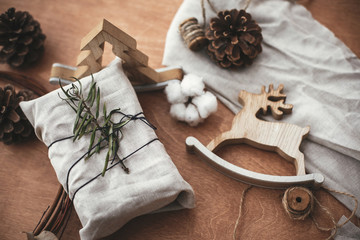 Merry Christmas, eco concept. Stylish rustic gift wrapped in linen fabric with green branch on wooden table with pine cones, reindeer, lights. Simple eco presents. Zero waste  holidays.