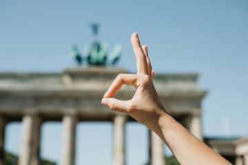 A person shows a sign with his fingers that means everything is good against the background of the Brandenburg Gate and blurry unrecognizable people in Berlin in Germany. © franz12