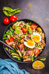 Tuna salad with pasta, olives, vegetables and egg in black plate on dark background.